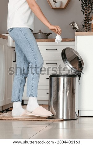Woman opening trash bin with her foot in modern kitchen Royalty-Free Stock Photo #2304401163