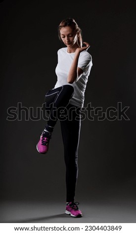 Blonde woman exercising, doing knee to elbow alternates, on black background, in tight dark pants, fuchsia sneakers, white t-shirt
