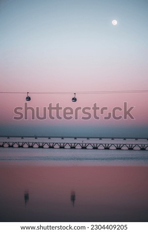 Lisbon; A low-key, vertical view of a beautiful scene featuring a full moon, pink sky sunset, the Tejo river, and a cable car. The overall effect is a serene and dreamy magical scene Royalty-Free Stock Photo #2304409205