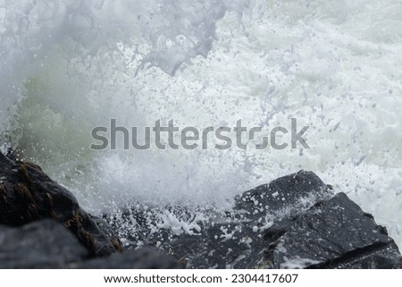 A powerful ocean wave crashing against the rocky shoreline, creating a spectacular explosion of white foam and spray.
