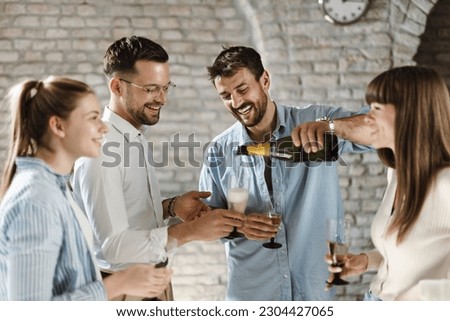 Young business colleagues pouring champagne during a party in the office