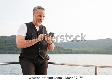 elderly man using smartphone on luxury yacht in summer