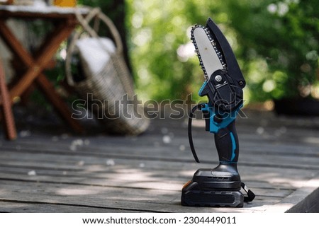 mini portable electric chain saw on summer garden background  Royalty-Free Stock Photo #2304449011