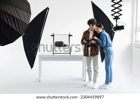 Team of professional photographer and his female assistant checking the pictures on photocamera while doing content photoshoot for modern bags