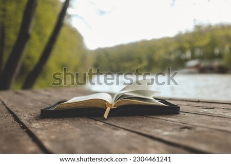 Open Bible on a wooden board near the river.