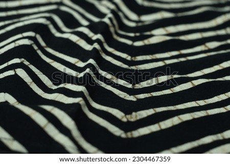 The fabric is thick natural cotton, black and white with yellow and black batik-style cravings. The napkin lies on a table against a black background in the studio. Tropical-inspired napkin.