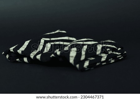 The fabric is thick natural cotton, black and white with yellow and black batik-style cravings. The napkin lies on a table against a black background in the studio. Tropical-inspired napkin.