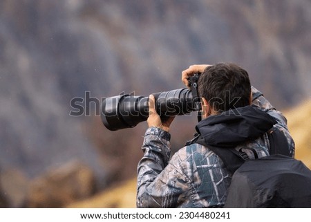 Nature photographer using a telephoto lens outdoors with his back turned and in a light drizzle