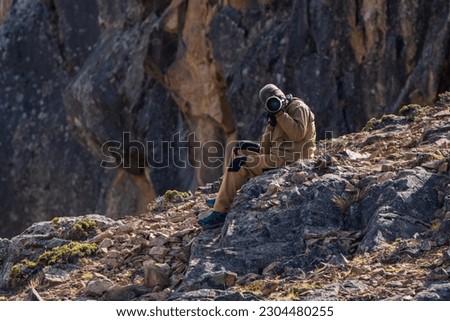 Nature photographer sitting on a rock taking a picture. Front view