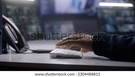 Close up shot of male security operator typing on keyboard. African American man works in police monitoring center. Big screens with CCTV cameras footage on background. Tracking and monitoring system.