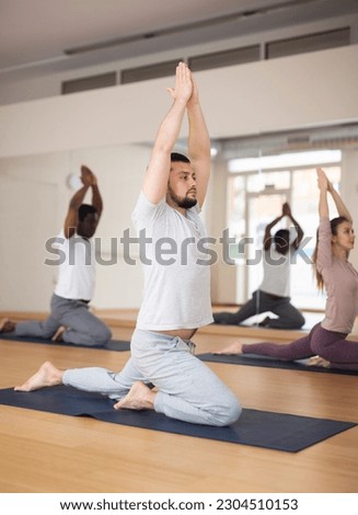 Sporty young man practicing Hatha yoga with group in modern fitness studio, making stretching exercises.. Royalty-Free Stock Photo #2304510153