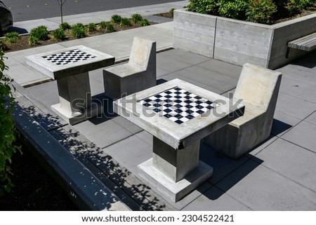 Cement chessboard tables, modern cement chairs and wooden benches in public park outdoor space

