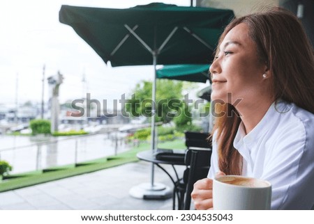 Closeup image of a beautiful young asian woman holding and drinking hot coffee in the outdoors cafe