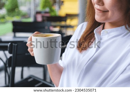 Closeup image of a beautiful young woman holding and drinking hot coffee in cafe