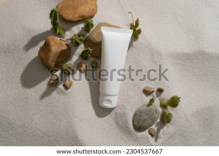 Against the beach sand background, an unbranded tube is displayed with some stones and small Cacti. Skin care branding mockup