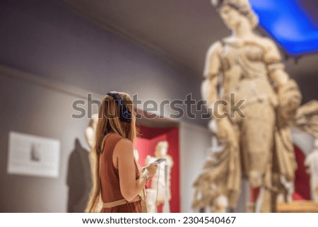 Portrait of contemporary young woman looking at sculptures and listening to audio guide at museum exhibition
