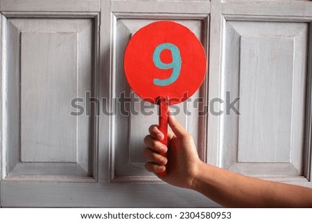 Number nine on the arm. Hand holding round wooden bulletin board with number 9 written on it