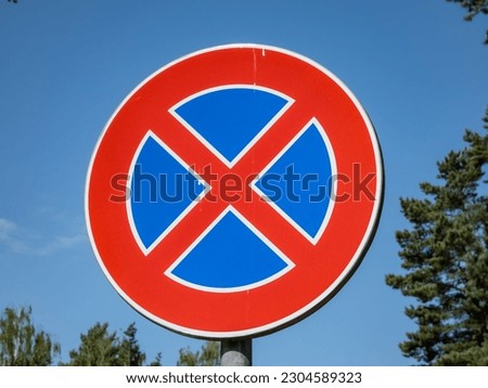 Metal signwith a red circle and red cross over a blue background outdoors with blue sky in the background. A sign indicates a clearway and means a parking prohibition