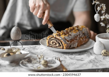 Man cutting poppy seed roll with knife. Festive table with poppy seed Easter cake, quail eggs, candles, spring branches.