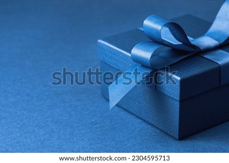 Luxury gift box with a blue bow on blue. High angle view monochrome close up. Fathers day or Valentines day gift for him. Corporate gift concept or birthday party. Festive sale