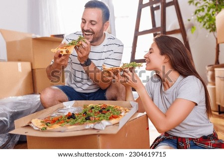 Couple in love moving in together, taking a break from unpacking cardboard boxes, having fun while eating pizza for lunch
