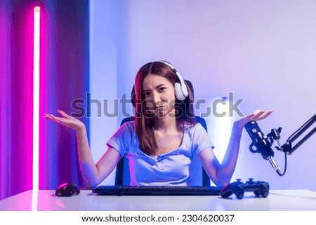 Professional gamer. Young asian pretty woman sitting on chair with computer pc in living room. Happy female Professional Streamer chinese wearing headphone playing game online in dark room neon light