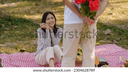 Happy romantic couple in Valentine's Day asian man hiding red rose flower behind for surprise his girlfriend