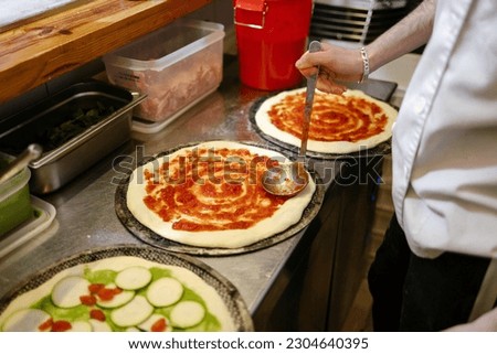 Detail shot of an unrecognizable pizza man's hands adding tomato sauce to a pizza in a pizzeria