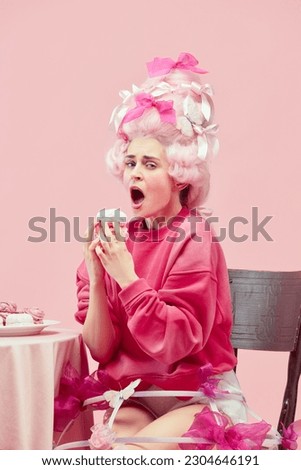 Sweet princess. Portrait hungry queen wearing big pink wig eating marshmallow with exciting face on pink studio background. Comparison of eras, modernity and renaissance, beauty, history concept Royalty-Free Stock Photo #2304646191