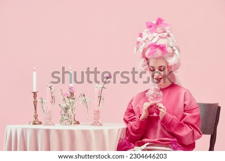 Portrait with fairy tail young princess wearing big pink wig holding wine glass with exciting face over pink studio background. Comparison of eras, modernity and renaissance, beauty, history concept