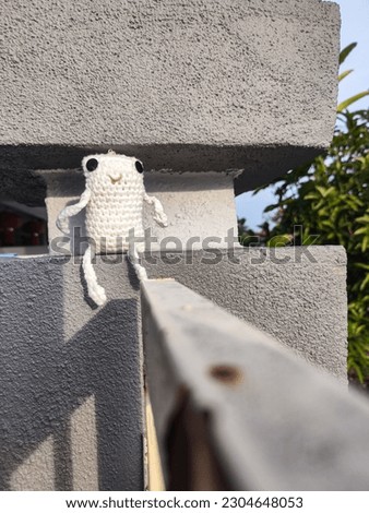A cute white frog-shaped doll was sitting on the wall of an iron fence.