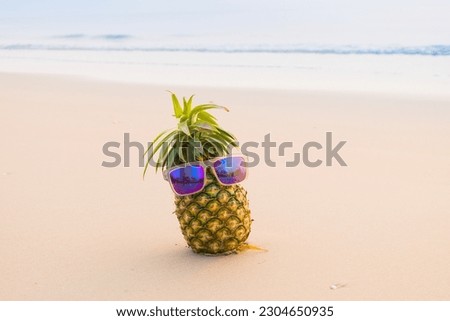 Funny pineapples in stylish sunglasses on the sand.