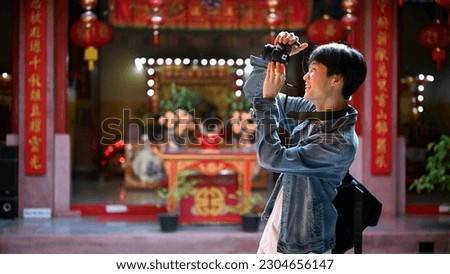 Handsome and happy young Asian male traveler is enjoying his solo travel trip in Thailand and taking photos in a beautiful Chinese temple.