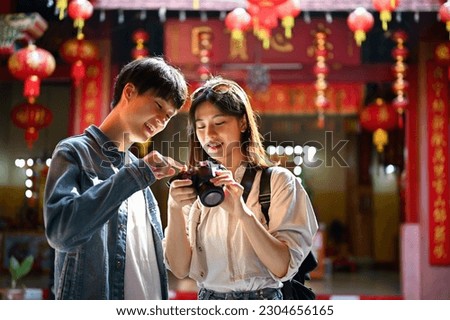 Smiling and happy young Asian tourist couple checking their photos on camera while visiting a beautiful Chinese temple together.