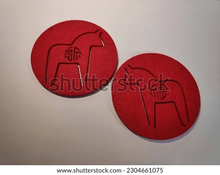 a pair of red coasters with a picture of a horse. Made of suede leather. low light setting. white background 