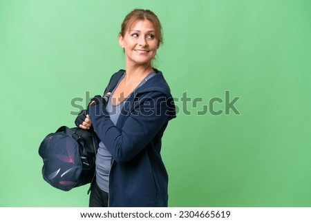 Middle-aged sport woman with sport bag over isolated background with arms crossed and happy