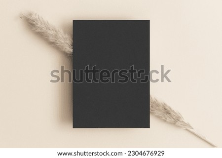 Black invitation card mockup with a pampas on the beige table. 5x7 ratio, similar to A6, A5.