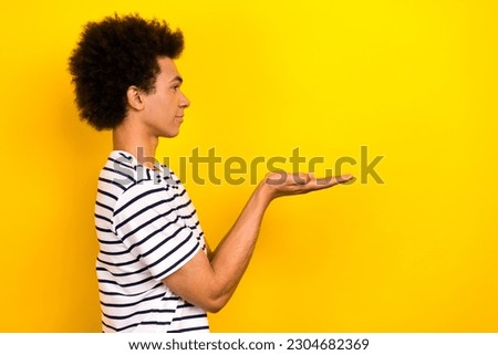 Profile portrait student guy stand side hold open palms donation wear striped t-shirt isolated yellow color background