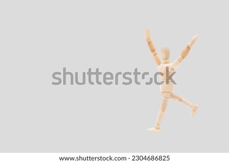 Photograph of a wooden mannequin with light gray background, it is in motion, with arms open and stretched upwards. Photo to be able to cut out. Concepts. Selective focus. Space for copy