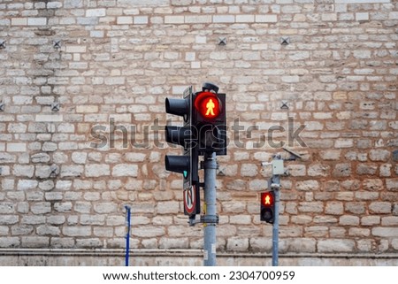 Pedestrian Traffic light showing red, a no-go sign that it is forbidden to cross the street. A traffic light with the historical wall in the background