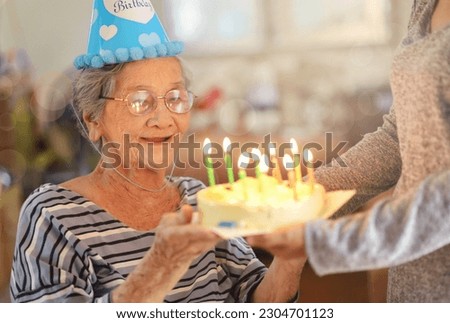 Senior woman celebrating birthday with cake, daughter surprise birthday cake for mother at home.