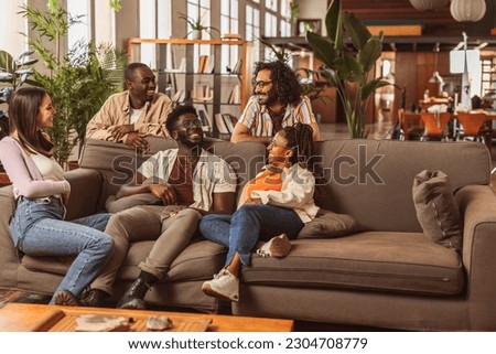 Team of young cheerful multicultural managers sitting on the couch in the office in front of their workplaces, creative people in modern office. Royalty-Free Stock Photo #2304708779