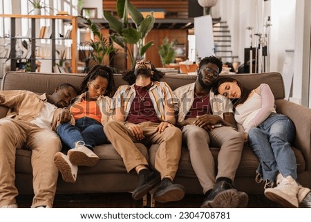 Party multiracial friends, drunk and hungover sleeping on a sofa in the living room after the celebration. Drinking, hangover and alcohol, coworking workers at break sleeping on the sofa