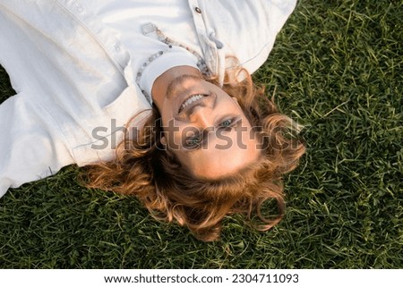 top view of young and happy man with long fair hair looking at camera while relaxing on grassy lawn