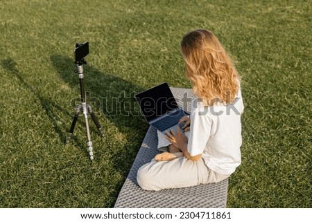 high angle view of long haired man using laptop near tripod with mobile phone during yoga lesson on green field