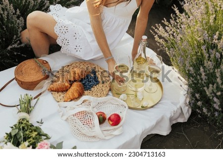 Girl in a summer dress, sitting with a glass of wine at picnic.	
Cropped picture of a woman sitting on a picnic on nature. Concept of having picnic on lavender field during summer holidays or weekends