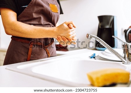 female slender figure in chef's work apron stands near kitchen sink, hands housewife dishwasher after washing dishes Royalty-Free Stock Photo #2304723755