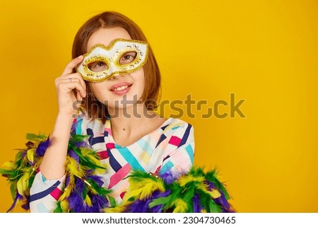 A joyful teenager girl wearing a colorful Brazil carnival mask, posing on yellow studio background, ready for celebration, birthday party, holidays concept