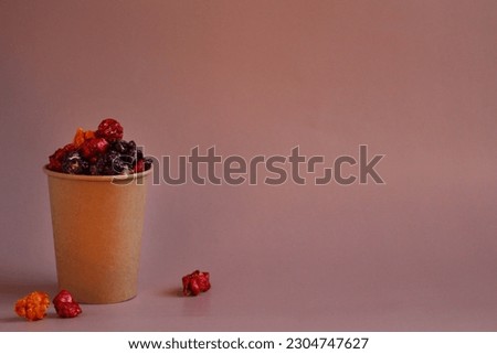 Multicolored popcorn in caramel glaze in a paper cup on a pink background