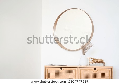 Part of a minimalist interior with a chest of drawers, a white vase of flowers, a beetle and a round mirror. Layout for the picture. Template for your design with copy space. High quality photo